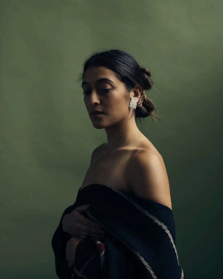 A woman in a shirt hanging off her shoulders with her hair in a bun and large silver earrings in.
