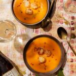 Creamy orange carrot and ginger soup topped with golden-seared scallops, chive oil, and pink peppercorns, served in dark bowls alongside glasses of white wine and a bottle of Tablas Creek Esprit de Tablas Blanc.