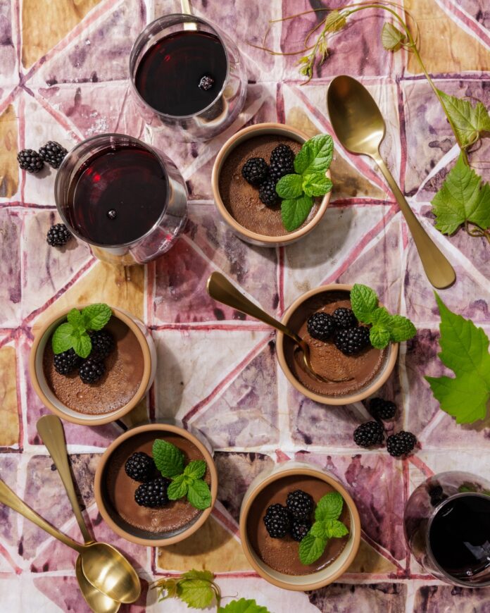 Rich dark chocolate pots de crème served in ceramic ramekins, topped with fresh blackberries and mint sprigs, paired with glasses of Janus Pinot Noir.