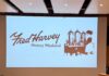 This Year’s Fred Harvey History Weekend Celebrates 150 Years of Legacy Audience sitting in an auditorium watching a presentation screen displaying the Fred Harvey History Weekend logo.