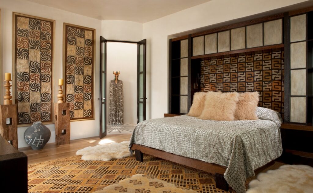 Master bedroom featuring a bed with a custom wood headboard unit, three framed tribal artworks from Papua New Guinea, a Tibetan rug, and sheepskin accents.