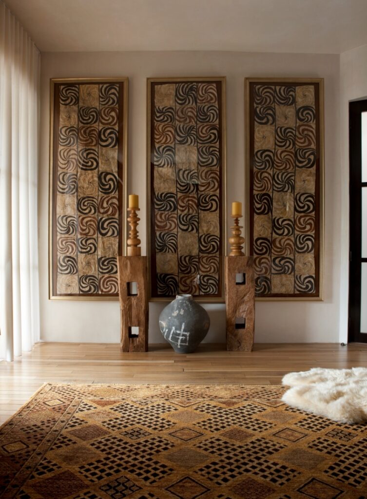 Detail shot of three large framed tribal textile artworks mounted on a neutral wall above a dark ceramic pot flanked by raw wooden pedestals.