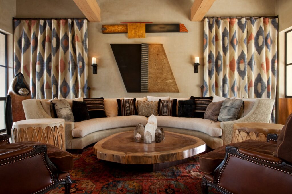 Living room sitting area centered around a large curved sectional sofa, a live-edge wooden coffee table, patterned curtains, and leather armchairs.
