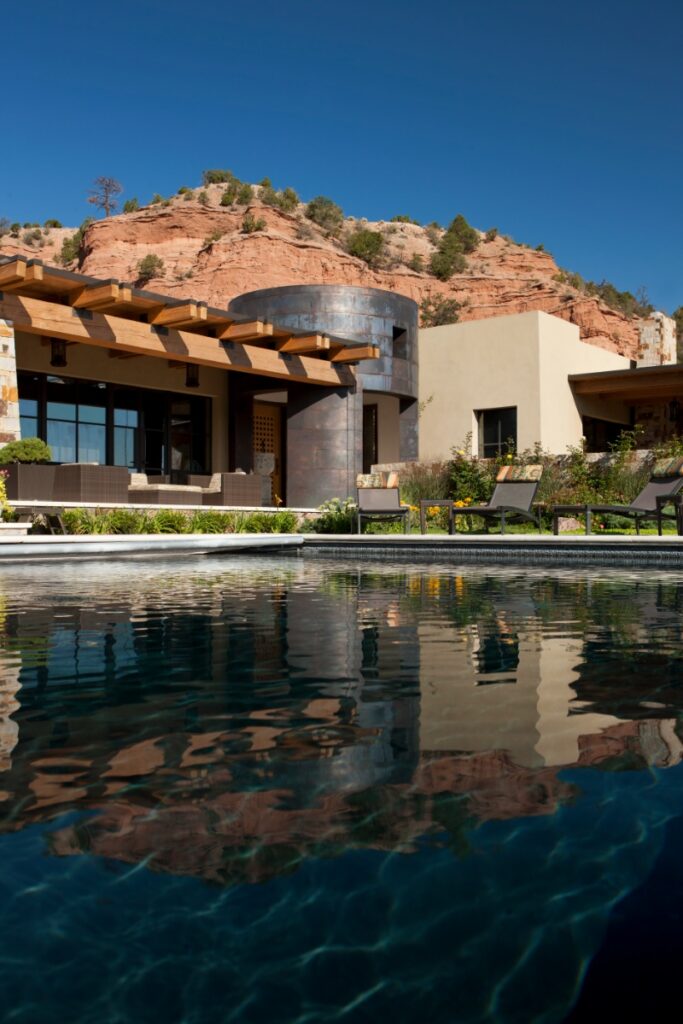 Exterior view of the contemporary home featuring warm plaster finishes, wooden pergolas, and a swimming pool reflecting the surrounding red rock hillsides.