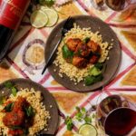 Seared lamb meatballs with wilted spinach simmered in a garlicky tomato sauce, served over giant couscous alongside glasses of red wine and a bottle of Kathryn Hall Cabernet Sauvignon.
