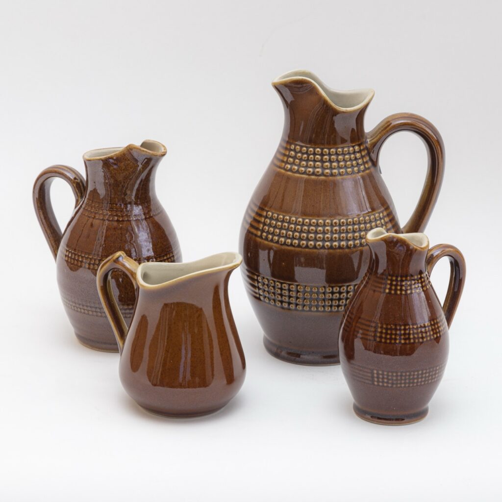 Four brown pitchers with spouts and large handles.