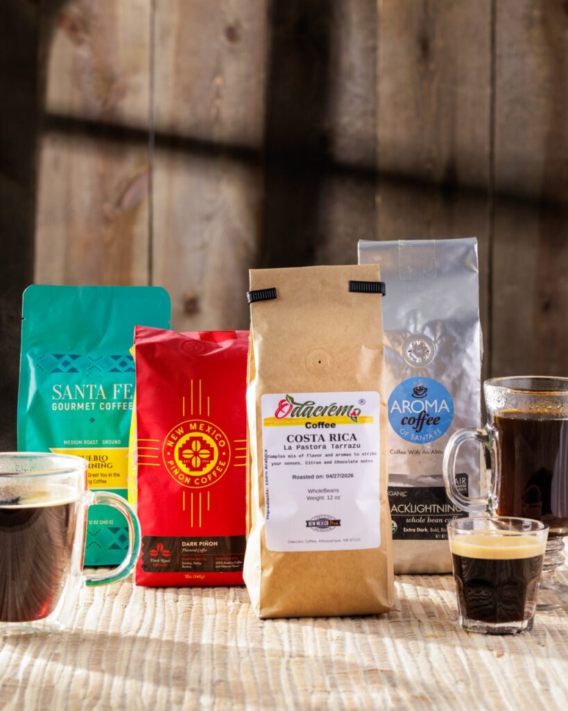Four bags of coffee in various colors beside cups and glasses of coffee.
