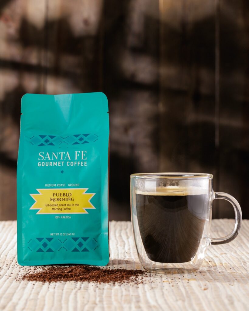 A glass cup of coffee beside a blue bag of coffee.
