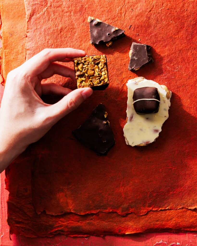 A person holds up a small square of chocolate by other pieces of chocolate.