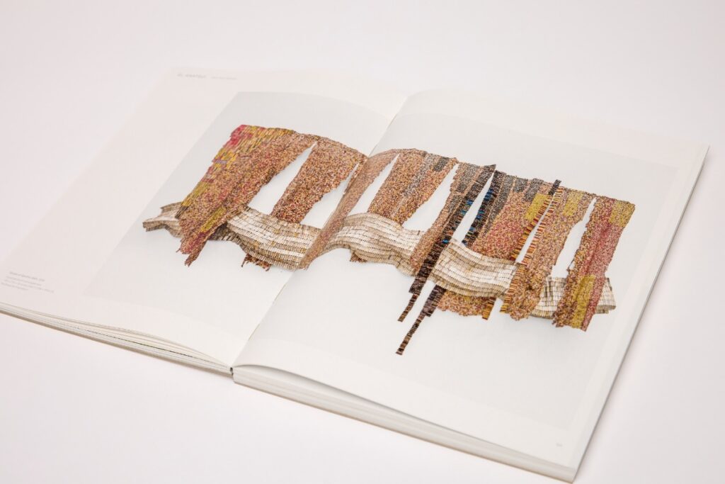 Open art book spread displaying an intricate, colorful woven textile artwork publication.