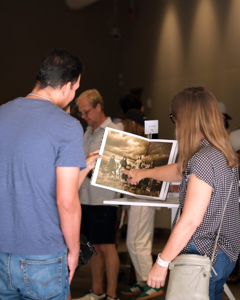 Artist Cara Romero pointing to a photograph in an open art monograph while talking with guests at a Radius Books event.