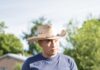 Faces of the Santa Fe Farmers’ Market: Meet Santa Cruz Farm A man in a grey shirt and beige hat standing in a field with a farm house behind him.