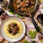 Slow-cooked beef stew braised with prunes, green Castellano olives, and orange peel, served over smooth polenta alongside glasses of red wine and a bottle of Ridge Lytton Estate Petite Sirah.