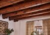 The Historic Applegate Estate Gets a Stunning Restoration Warm living space styled by French & French, featuring heavy dark wood ceiling beams, striped armchair seating, neutral curtains, a Native American wall hanging, and a small kiva fireplace.