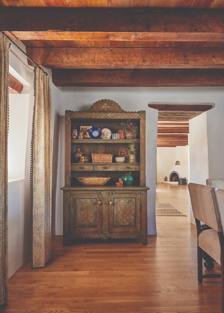 A custom vintage-inspired wooden cabinet set against clean white adobe walls and exposed wood ceiling joists in a bright, open entryway.