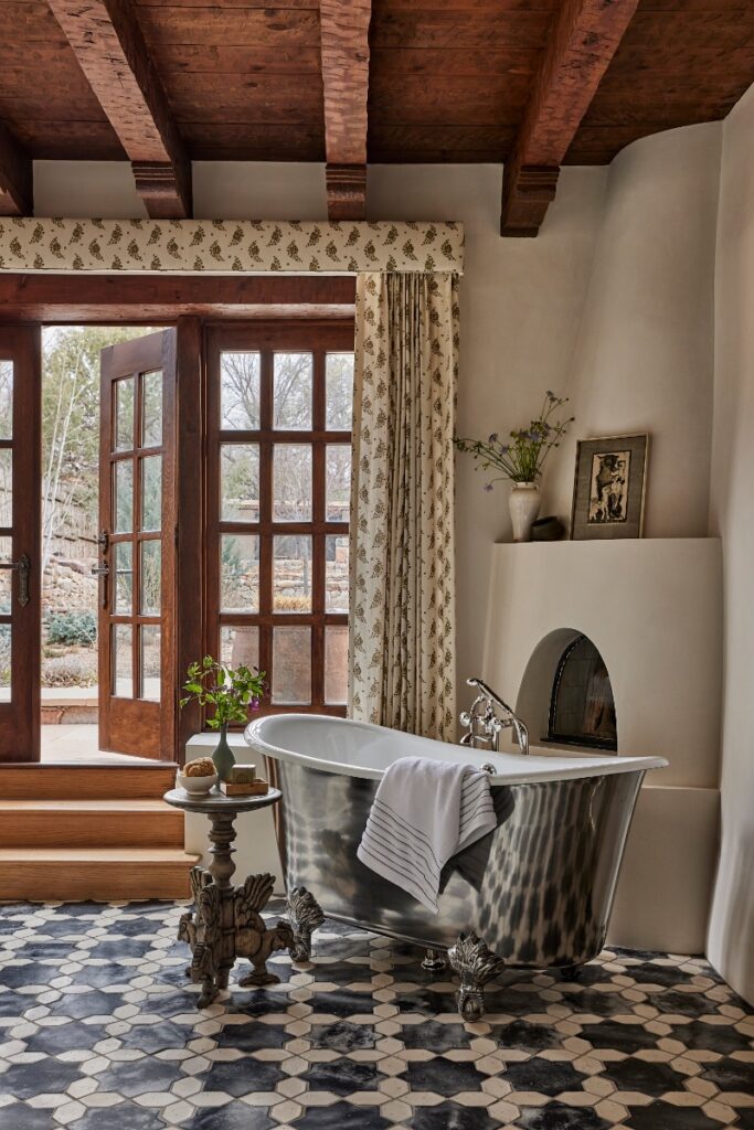 Elegant bathroom featuring a freestanding polished metallic soaking tub, patterned floor tile, a corner kiva fireplace, and french doors leading out to the patio.