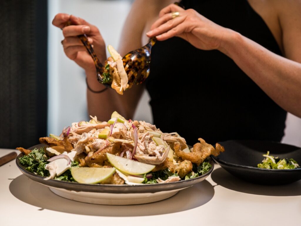 Close-up of a guest serving "The Harvest Moon" salad using tortoiseshell servers from a large serving bowl.