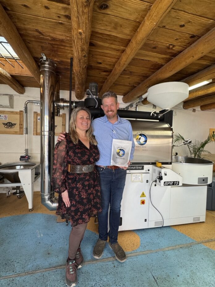 The owners of Wolf and Mermaid Enchanted Cafe stand side by side in the cafe space, holding an award in the man's hand.