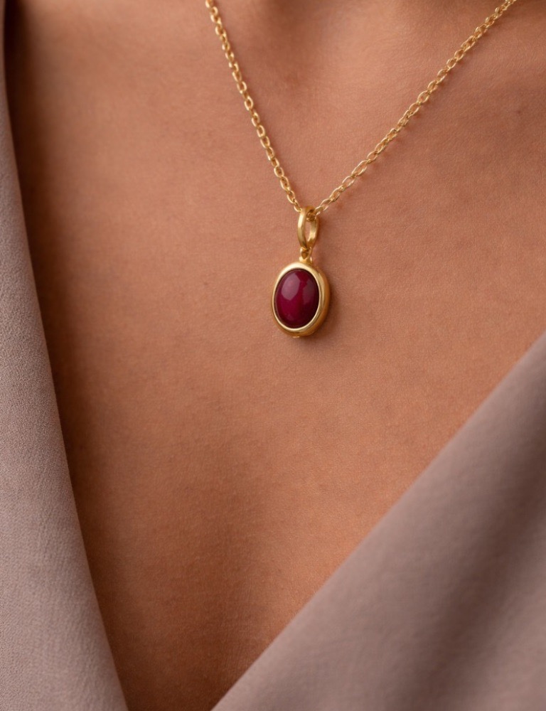A woman wearing a red ruby necklace on a gold chain.